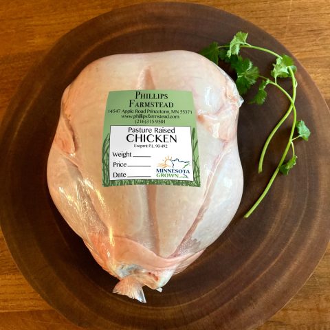 A package whole raw chicken on a wood plate with a Phillips Farmstead logo.