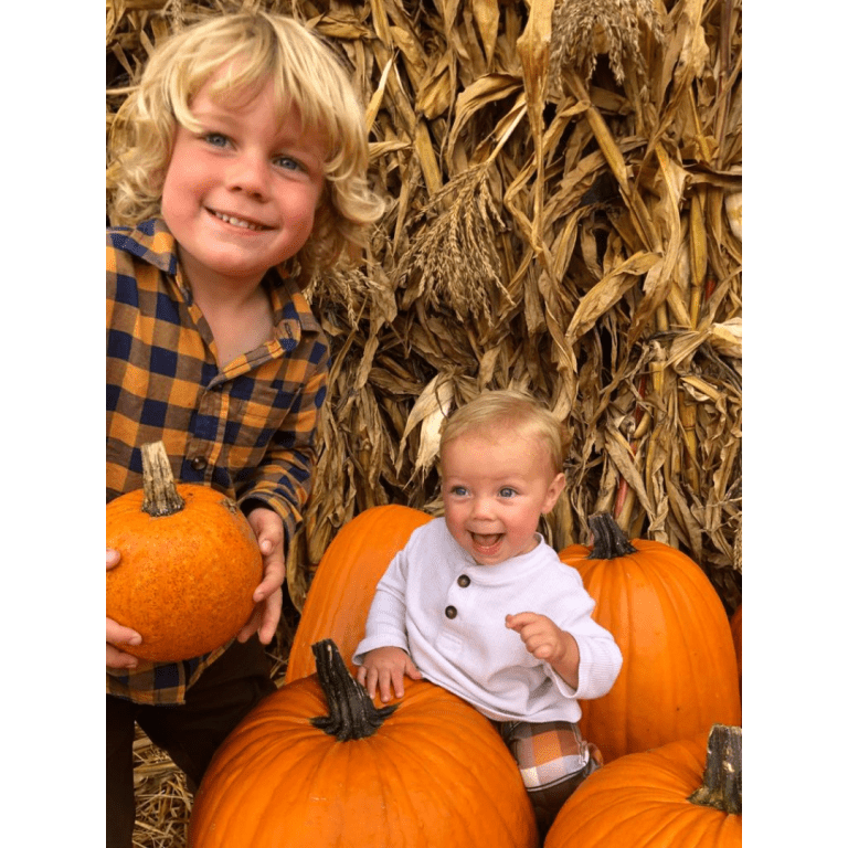 two children holding pumpkins in front of corn shocks