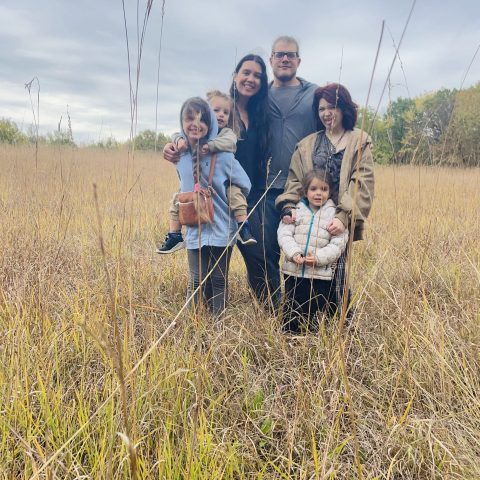A farm family of six people standing in a golden field.