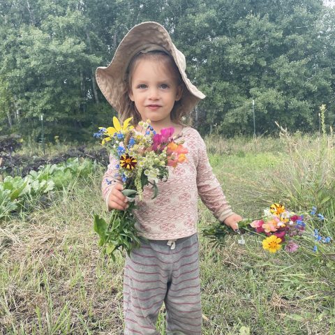 Gril with floppy hat holding flowers in a field.