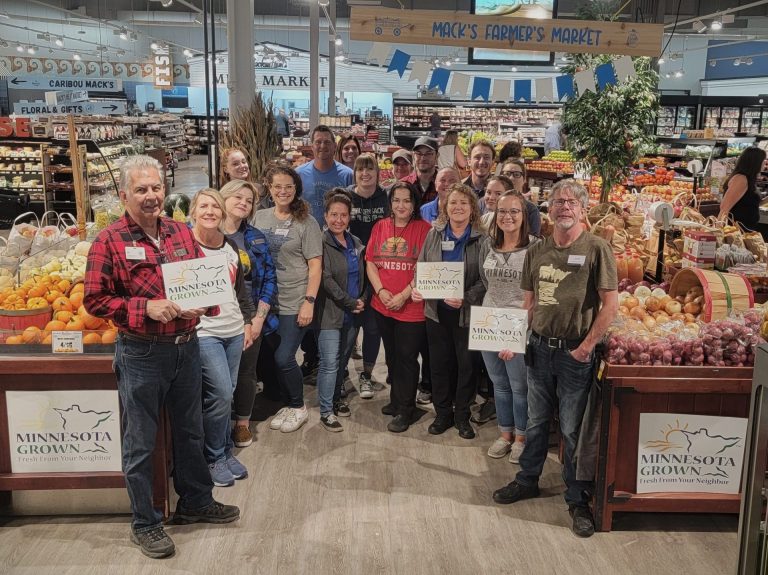 A group of grocery store staff gathered in their produce display. Many of them hold Minnesota Grown signs.