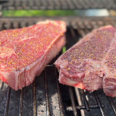 Two raw, seasoned steaks on a grill.