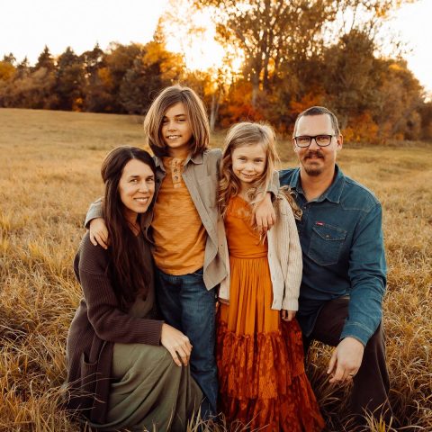 Family of four smiling and embracing in a sunny field