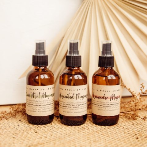 three glass bottles of magnesium spray sit on a wicker table with a beige background