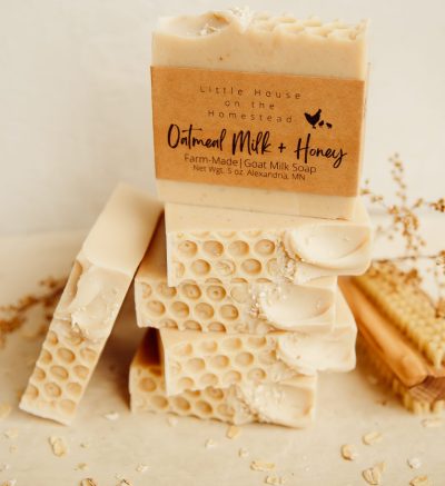 Beige bars of oatmilk and honey goatmilk soap are stacked on a beige surface. The bars have a honeycomb pattern in the top and a paper label.