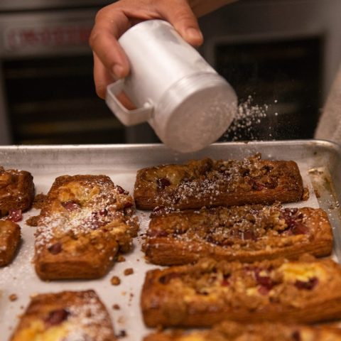 Picture of someone sprinkling powdered sugar on pastries in a baking pan.