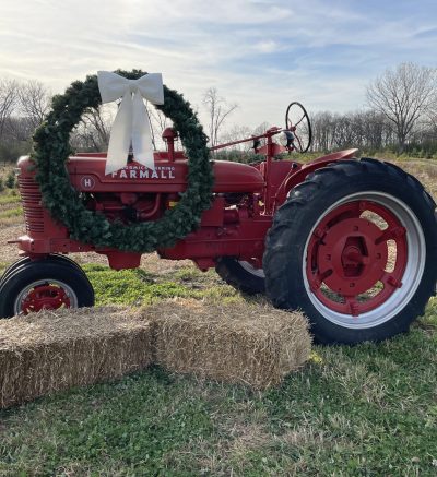 A picture of a tractor surrounded by straw hay bales and a wreath drapped over it.