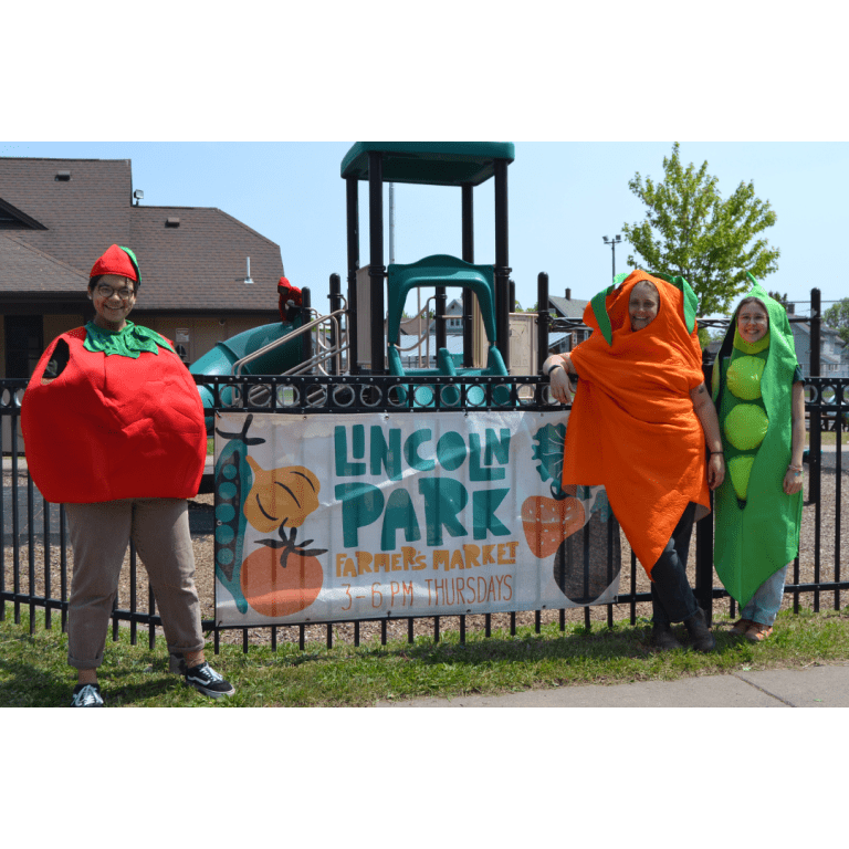 Lincoln Park Farmers Market sign surrounded by people dressed in veggie costumes
