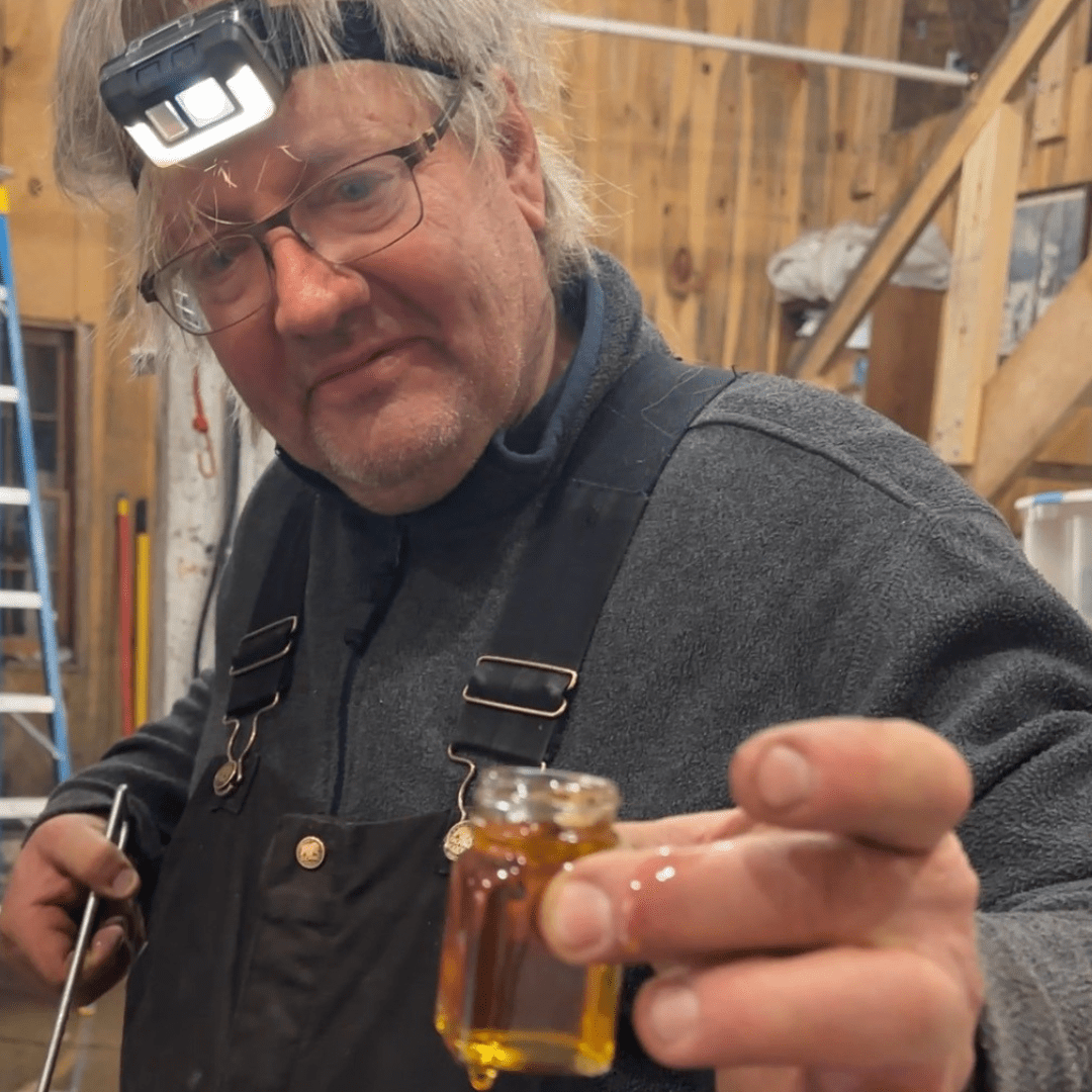 A man holding a small bottle of maple syrup that he is testing for sugar content.
