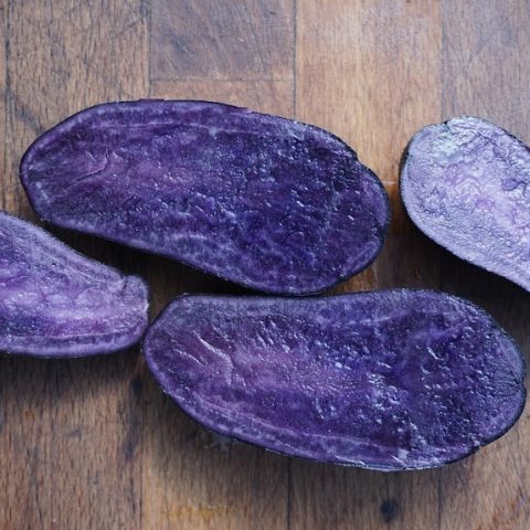Two purple yams/squash cut in half against a wood background.