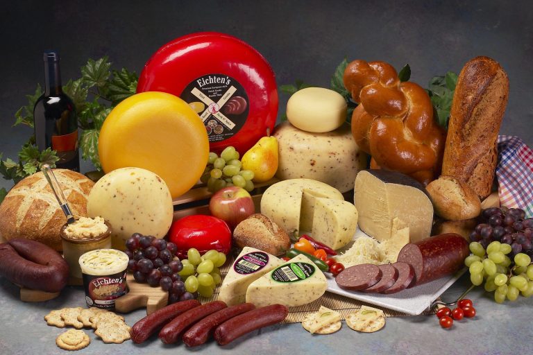 Spread of wheels of cheese, wedges of cheese, bread, sausages, fruits, and more.