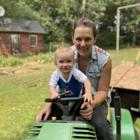 A mom and baby sit on a green tractor outside.