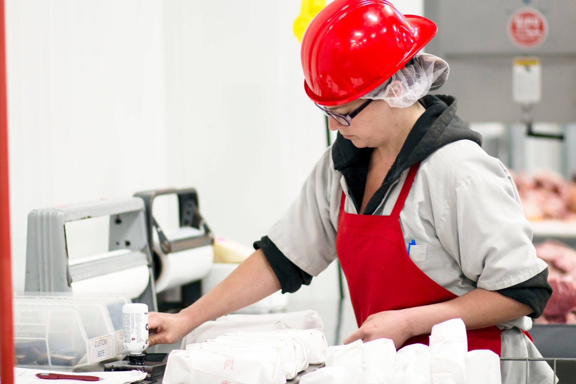 A worker in sterile clothing and hat packaging meat.