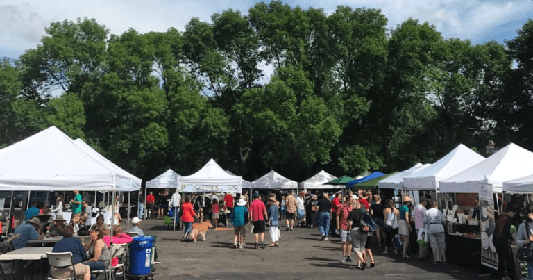 Image of a farmers' market with white tents and lot of people shopping.