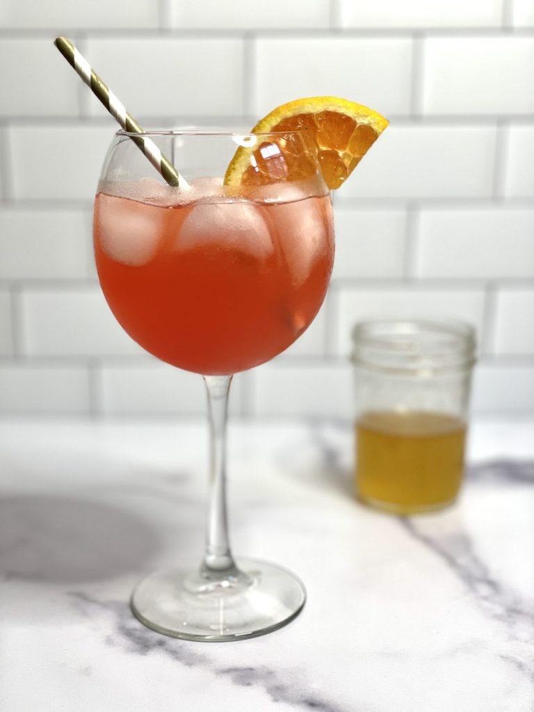A wine glass filled with a dark pink cocktail garnished with an orange slice.
