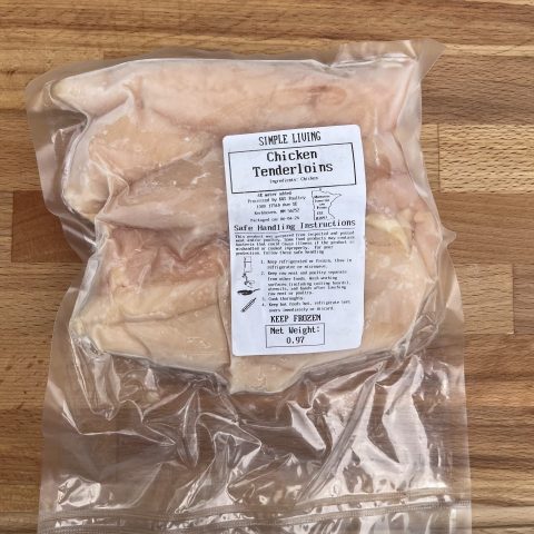 A picture of packaged raw chicken tenderloins against a wood cutting board.