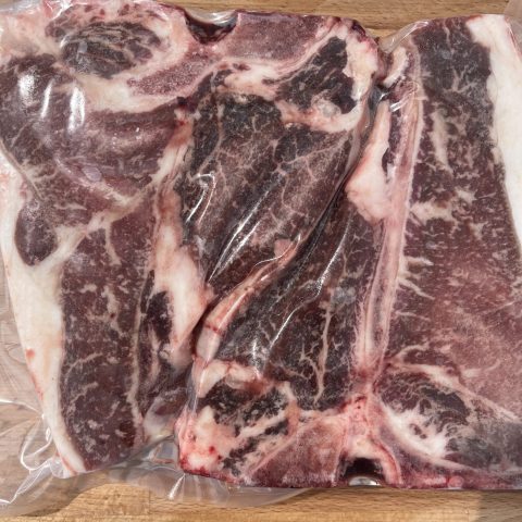 A picture of a packaged raw red meat against a wood cutting board.