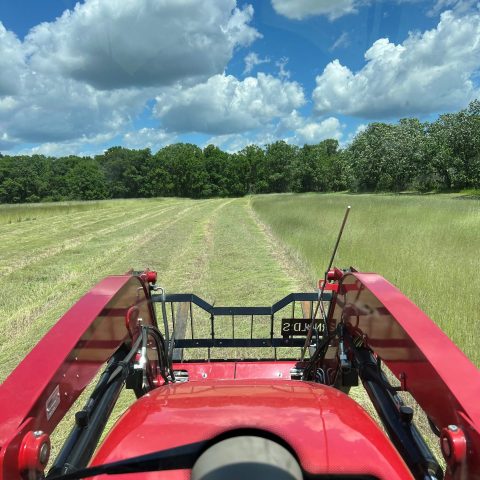 A view from the cab of a tractor looking out at the back of the red tractor and a field beyond.