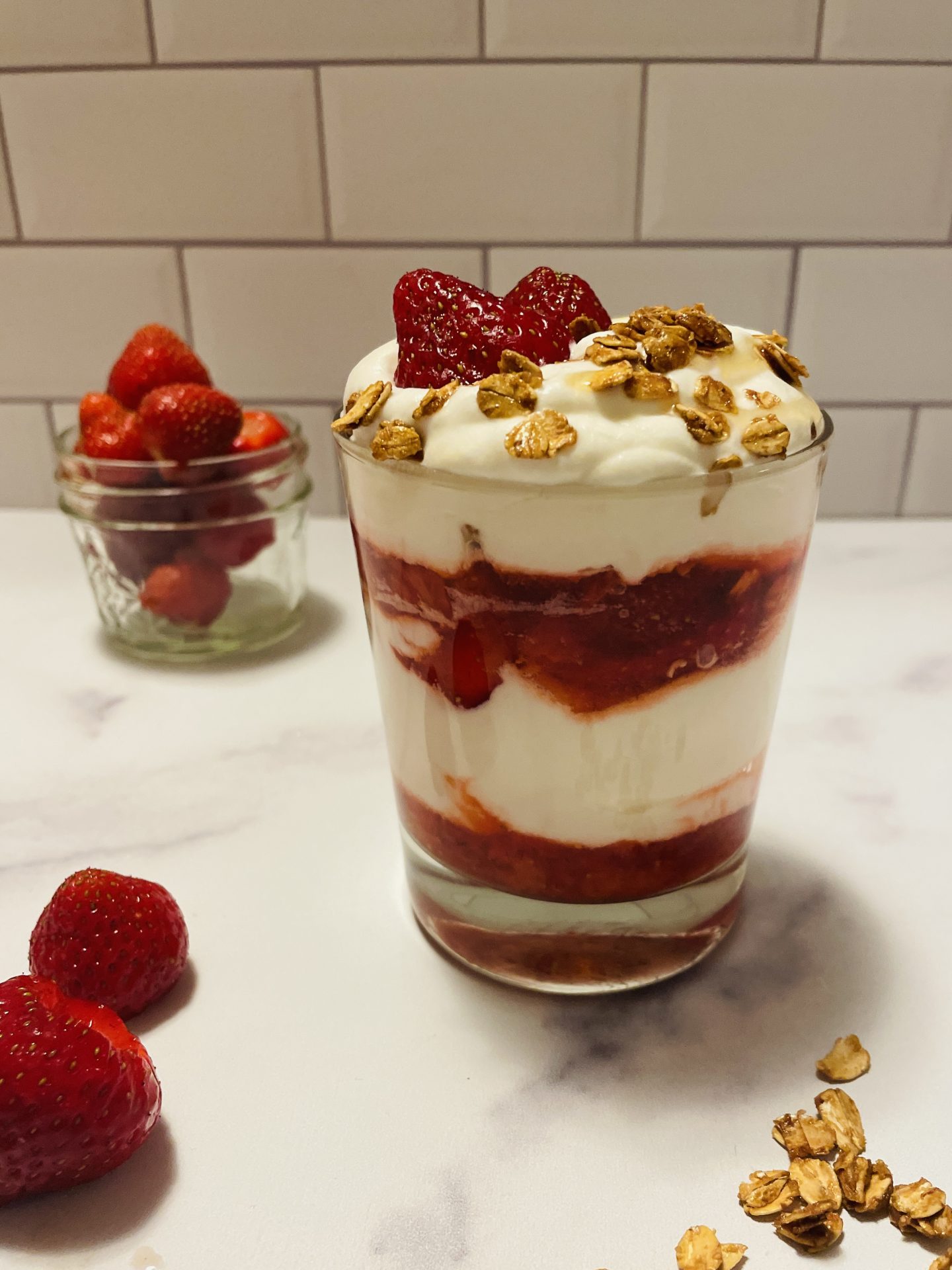 A lowball glass filled with layers of strawberries and whipped cream, topped with oats.