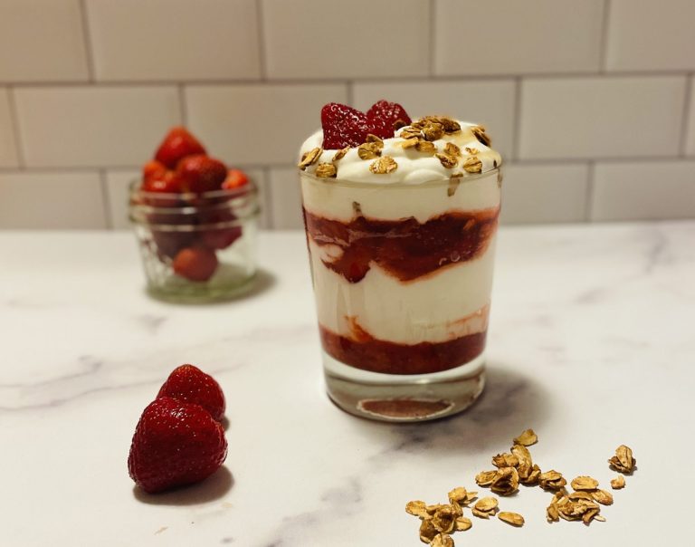 A lowball glass filled with layers of strawberries and whipped cream.