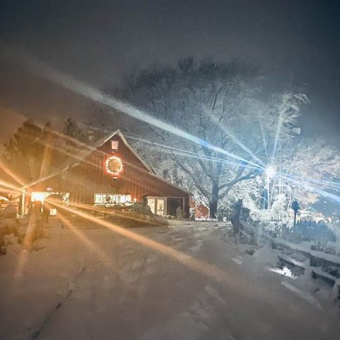 Picture of a barn at night in the snow with bright lights.