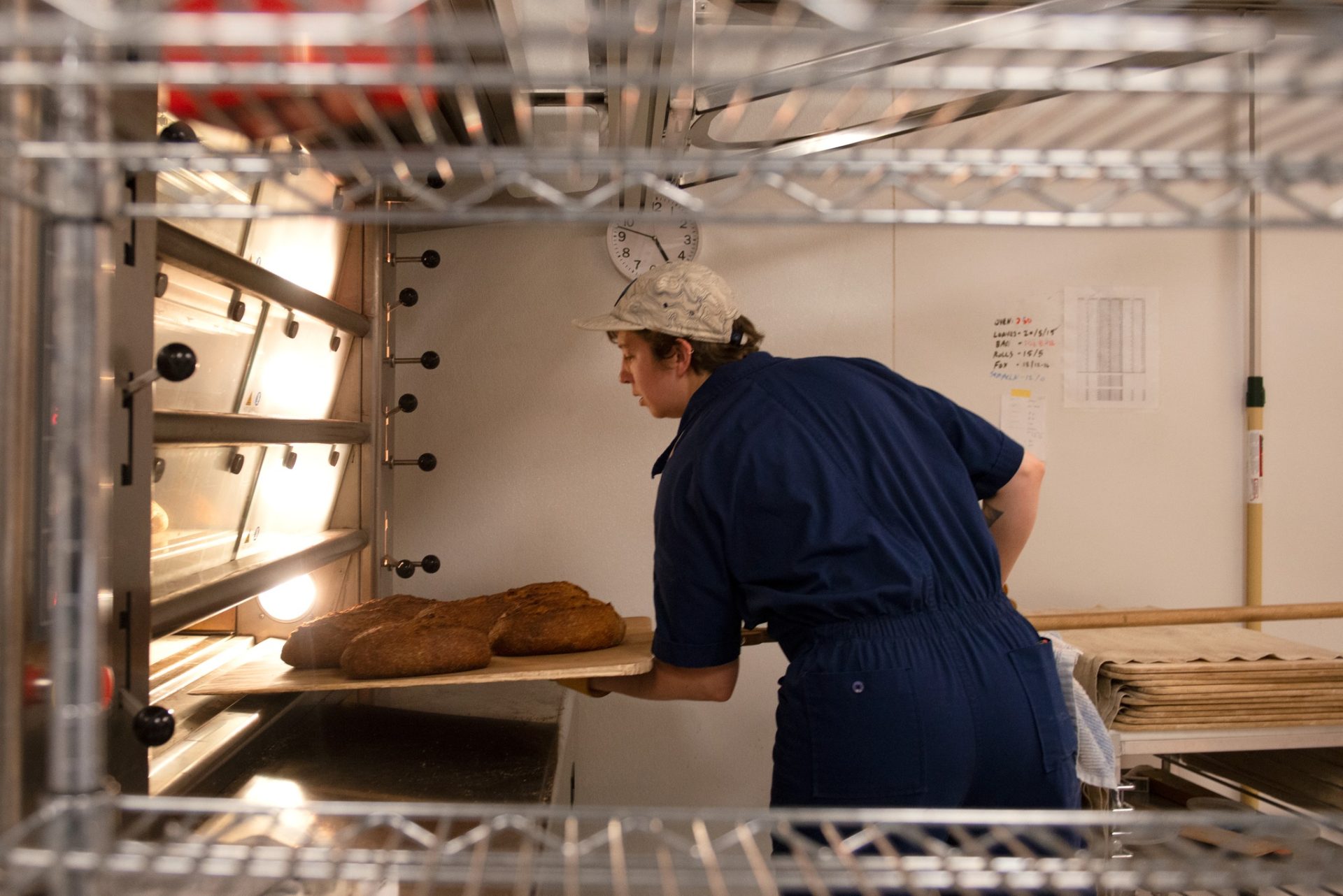 A baker putting several loaves of bread into an oven using a large wooden peel.