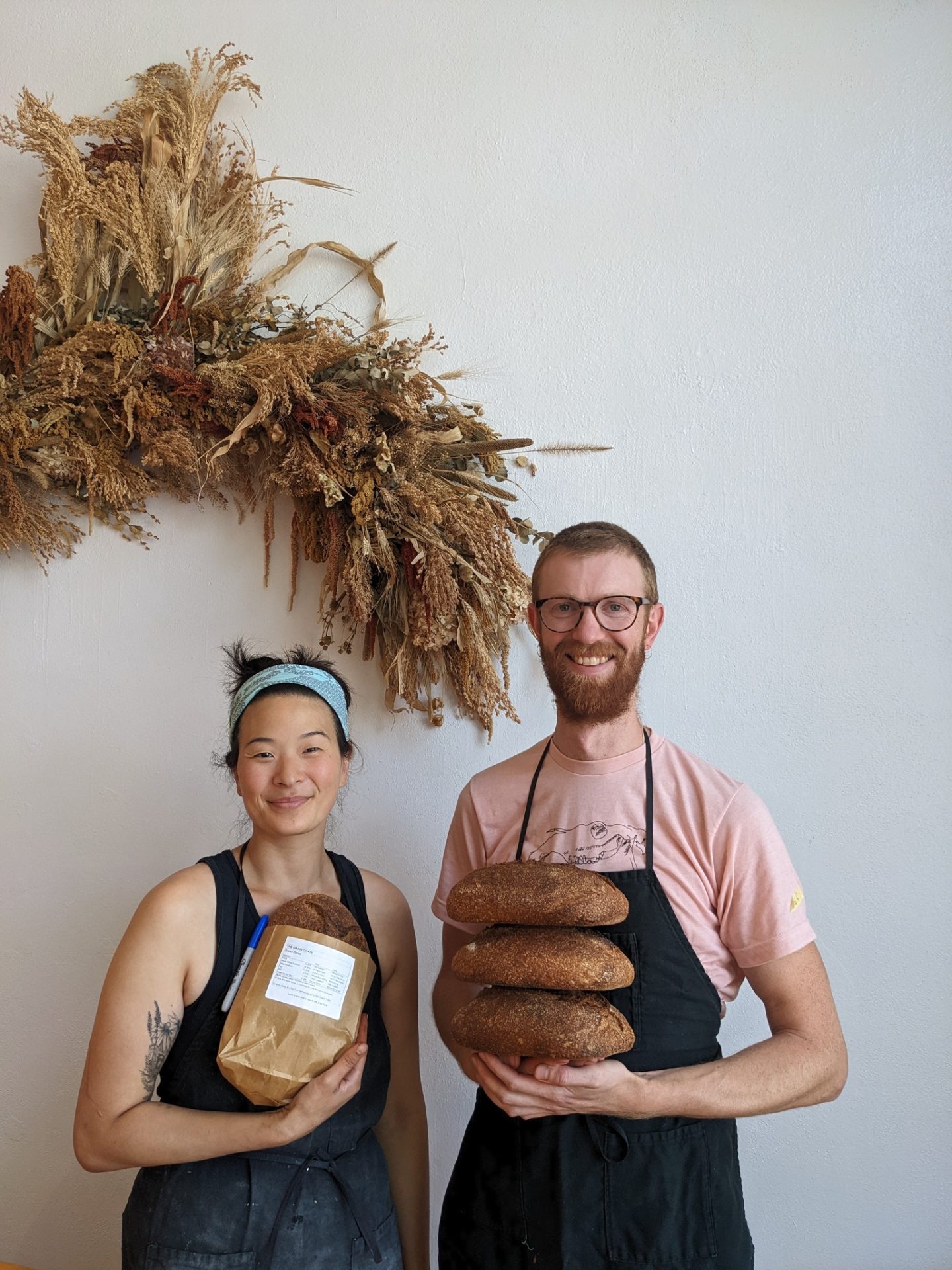 Two bakers, a man and a woman, holding loaves of bread.