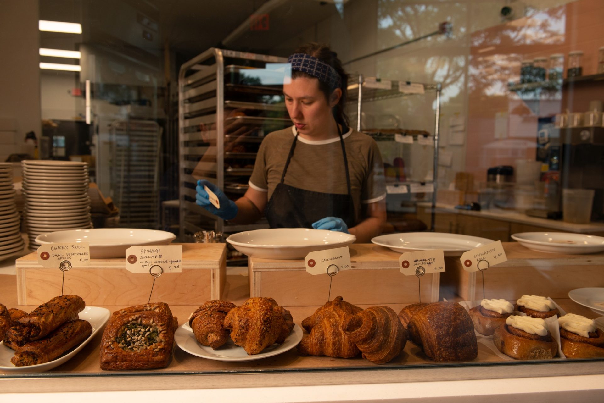 A woman stands behind a pastry case filled with baked goods.