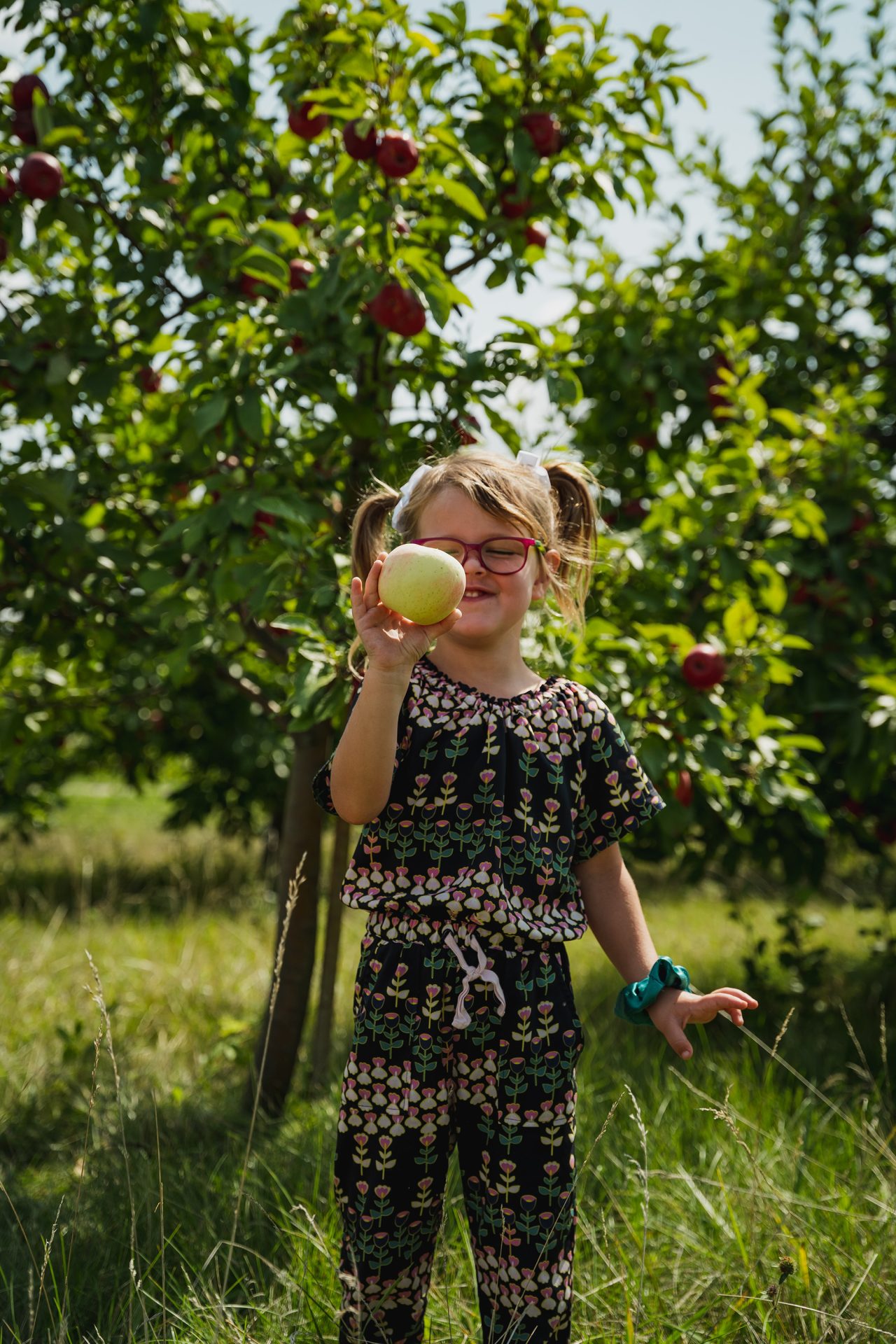 Girl in an orchard holding an apple.