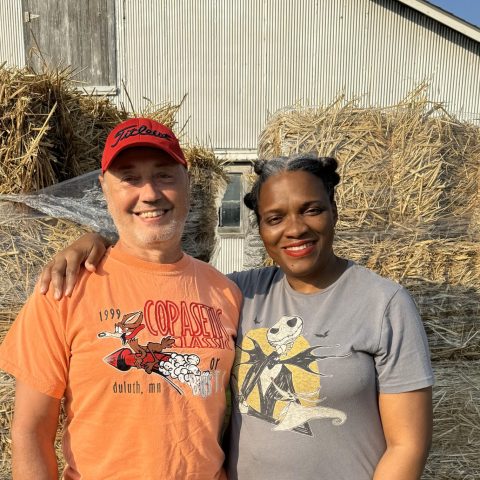 Two farmers in front of their barn with straw bales.