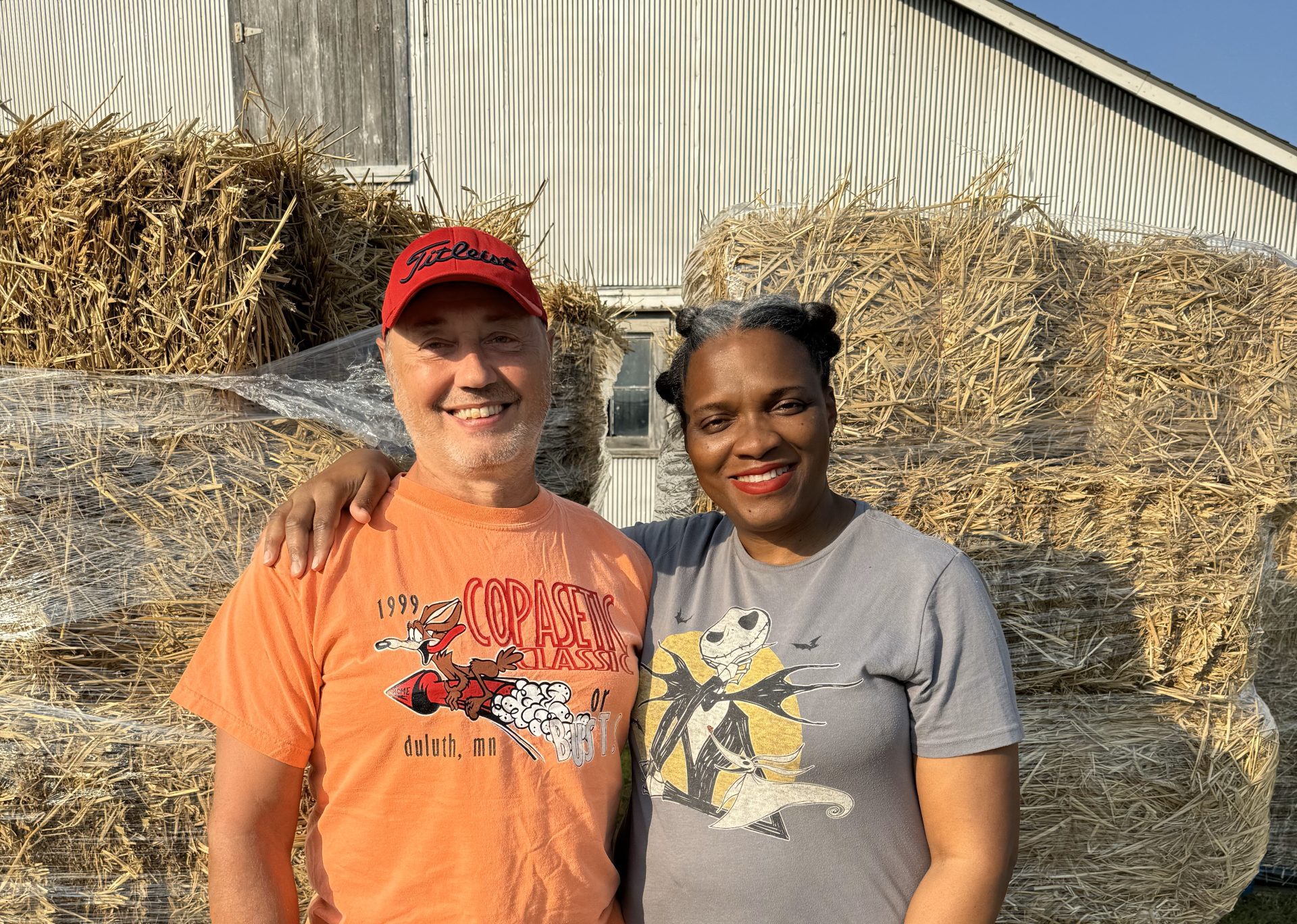 Two farmers in front of their barn with straw bales.