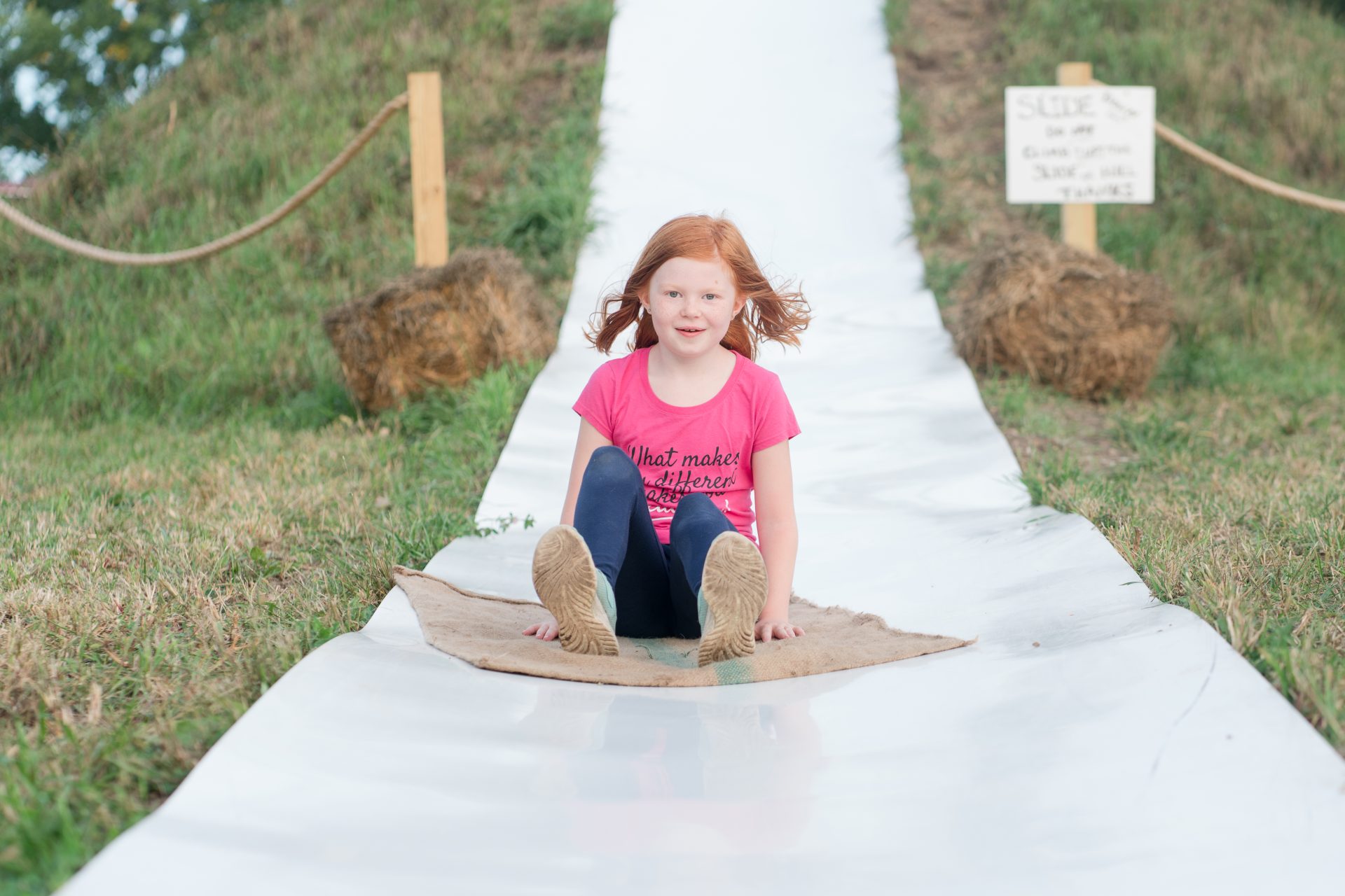 A girl in a pink going down a long slide on a grain bag.