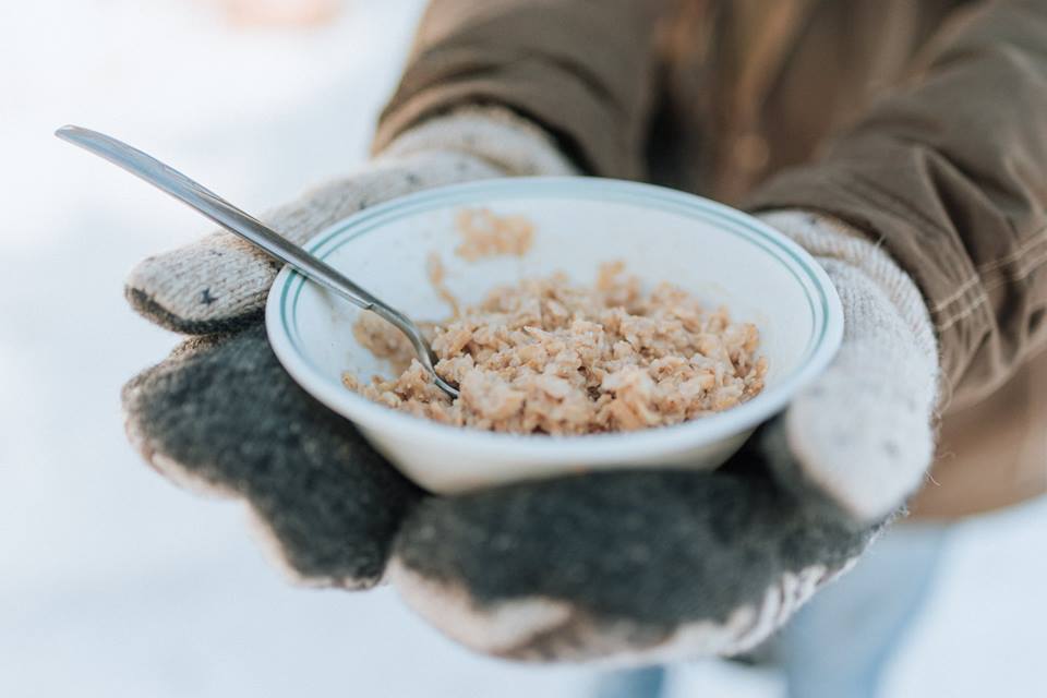 A closeup picture of a pair of gloved hands holding a warm bowl of locally grown oatmeal outside in the snow