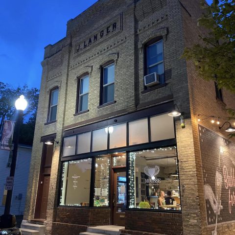 pale cream brick building at night. mousse logo on the front window, JLANGER is in brick on the front facade, the mural peaks out on the side