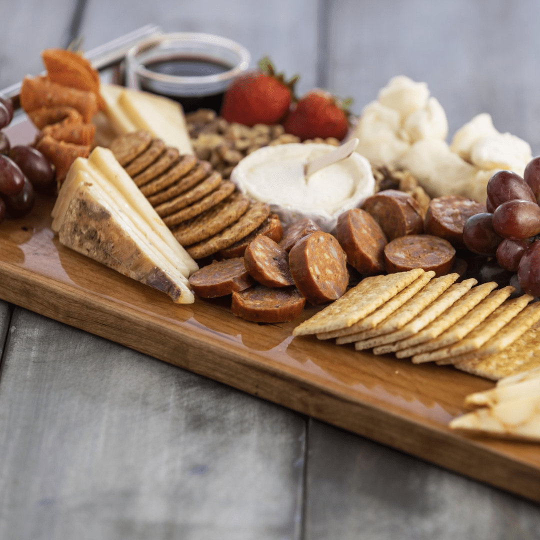 Picture of a wood board of crackers, sausages, cheeses, dips, and fruits.