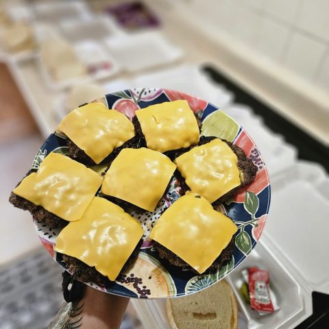 Picture of a plate of burger patties with yellow cheese on top of each.