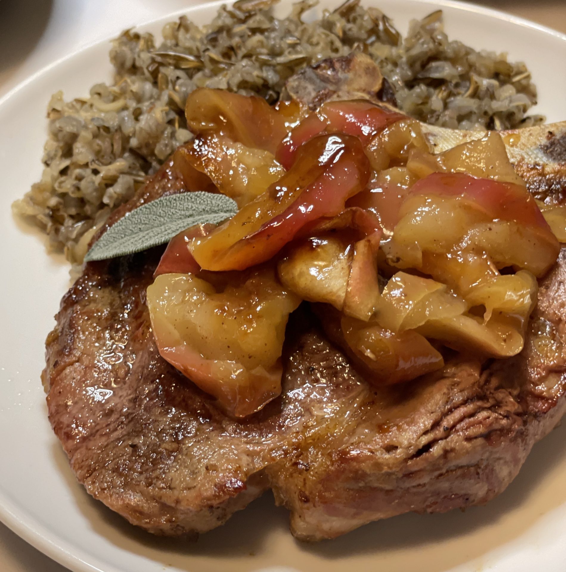 Close up of a pork chop on a plate topped with baked apples and served with wild rice.