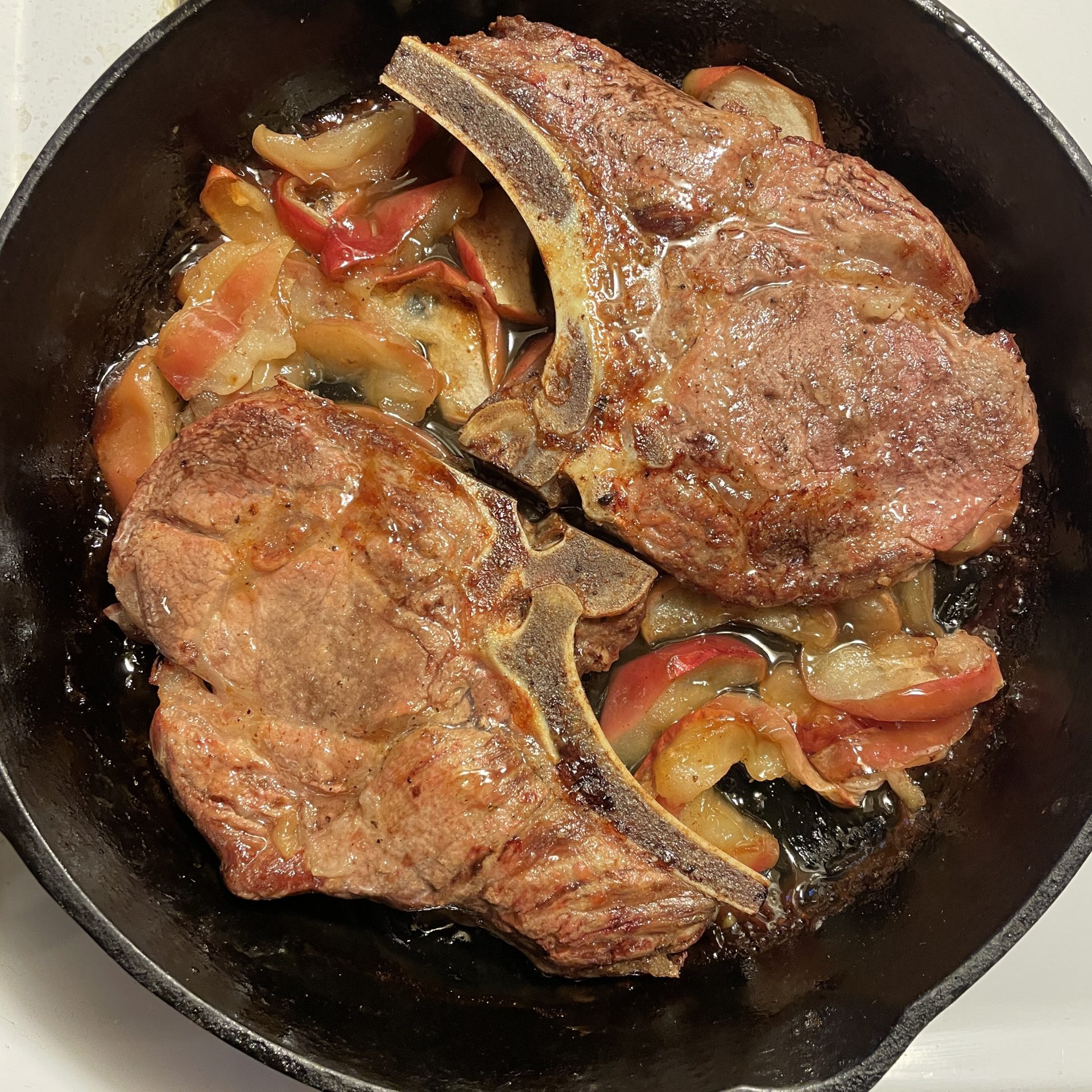 Two baked pork chops baked with apples in a cast iron pan.