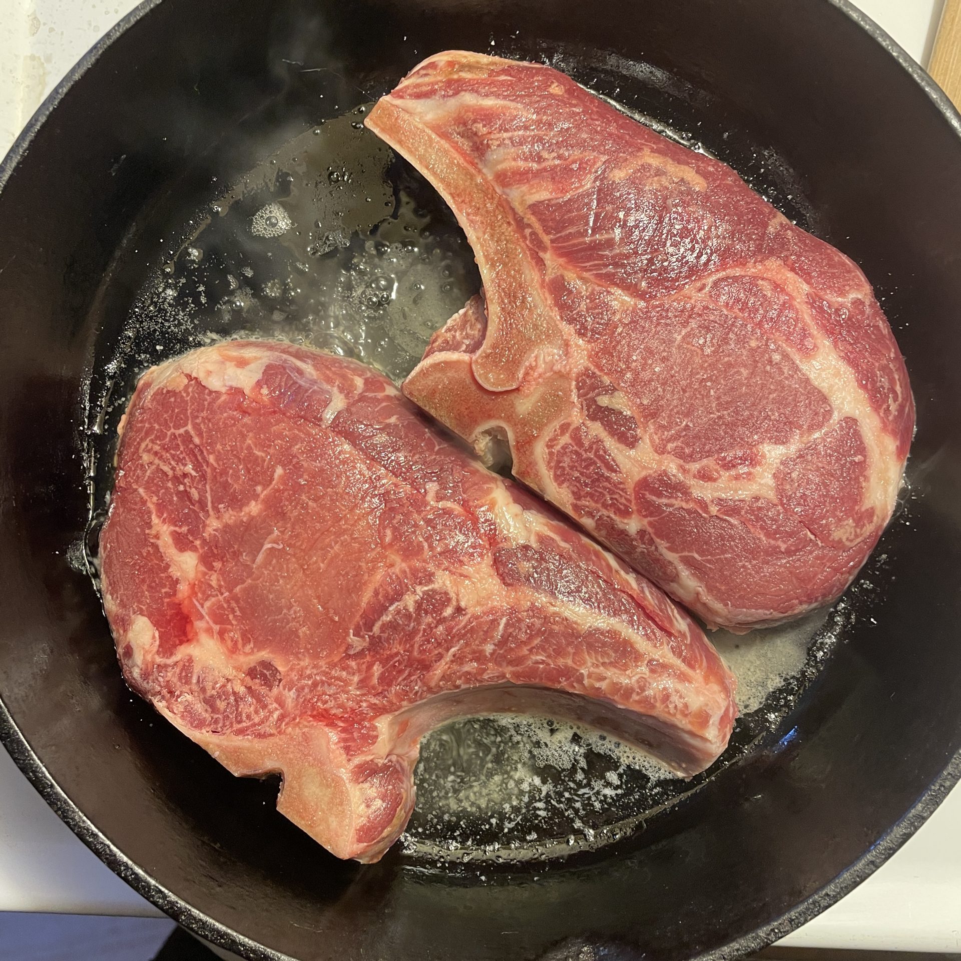 Two bone-in pork chops in a cast iron pan.