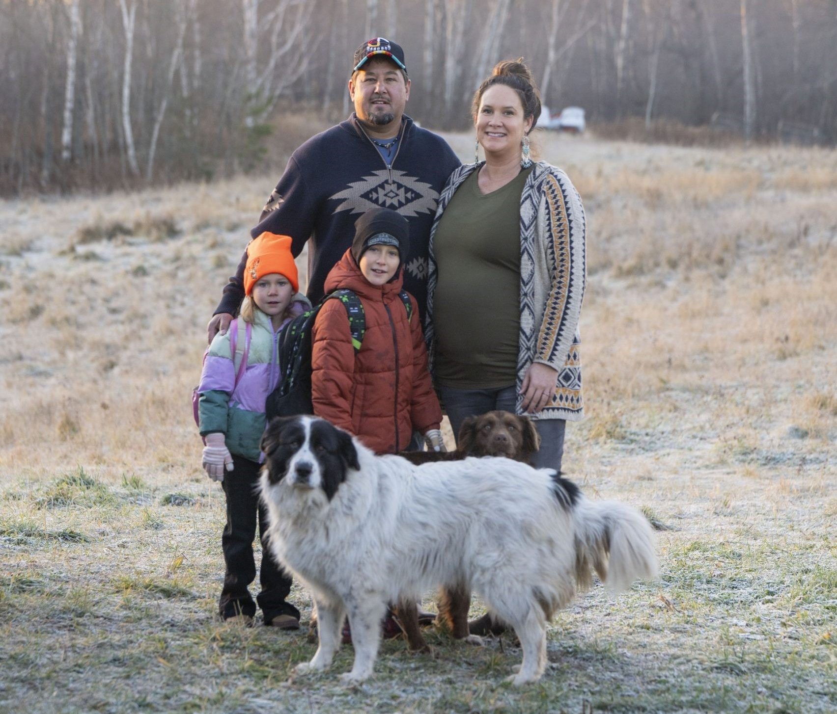 Two adults, two children and a dog stand together in a field in late fall