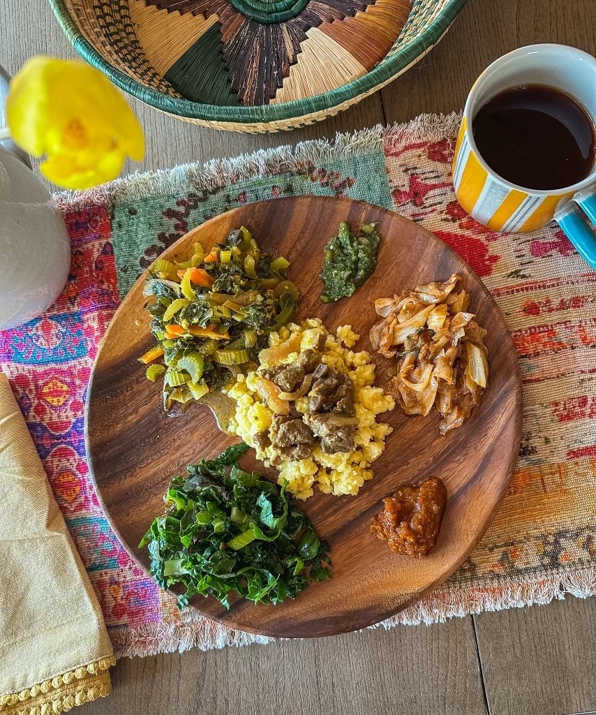 Overhead photo of wooden plate on colorful placemat. Plate is filled with greens, beef and onions over a cornmeal dish, and chutneys and sauces.