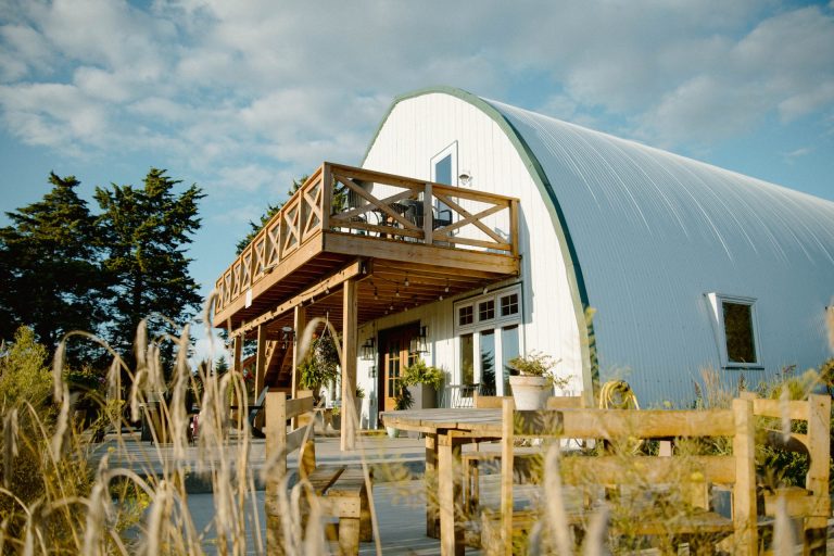 Picture of a white barn with a deck with a long, golden grass in the foreground.