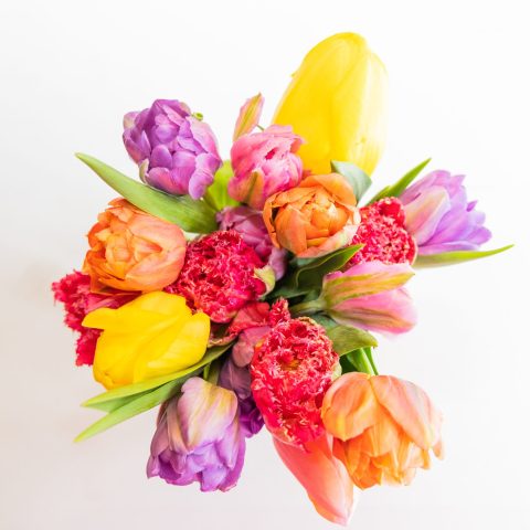 Picture of a vibrant spring flower bouquet against a white background, featuring yellow, orange, purple, and pink flowers with greenery.