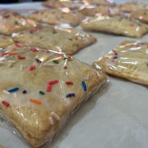 Closeup picture of a tray of frosted baked goods with sprinkles.