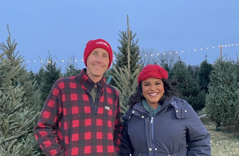 a man and woman smile in a tree farm