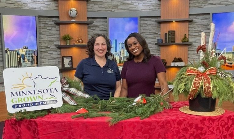 two women smiling at a table full of holiday greenery, a sign reads minnesota grown