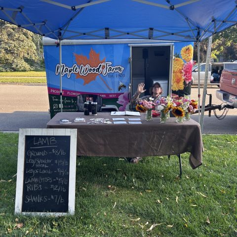 man sits at a farmers market stand behind a table full of flowers