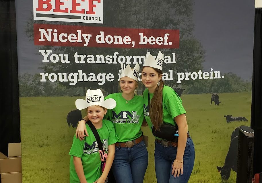 Three girls of different ages in front of a sign for Minnesota beef.