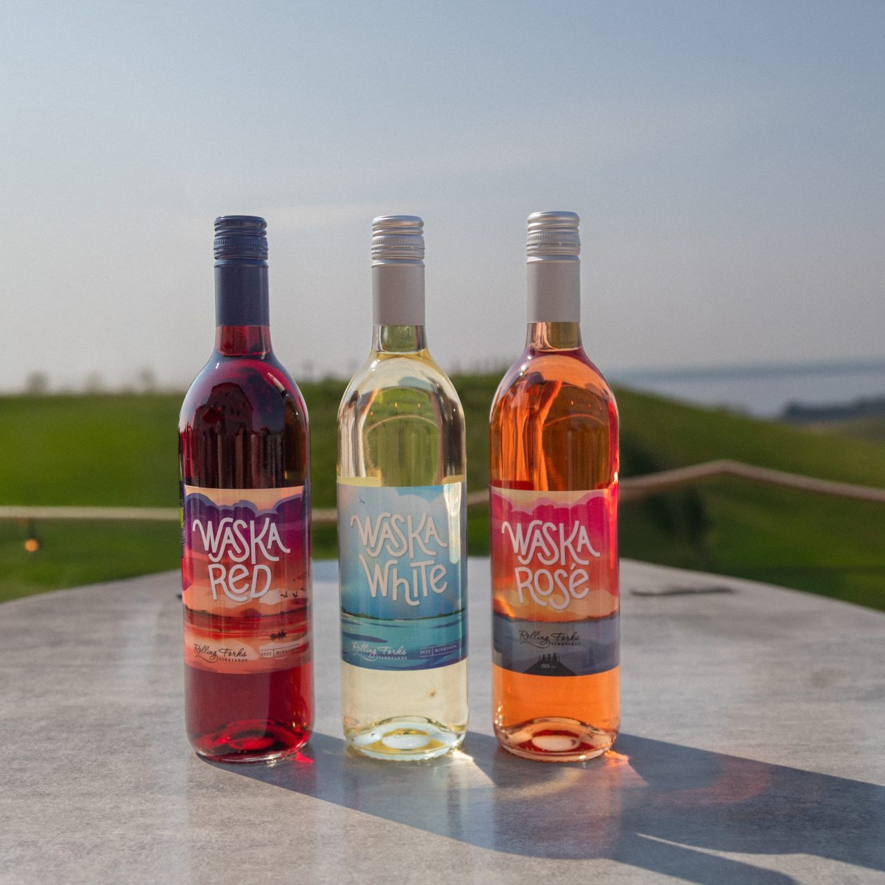 three wine bottles on a stone table, the background is a green lush vineyard
