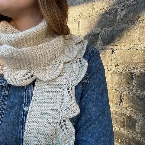 shot of a womans chect ina blue shirt, a white knit scarf with scallopped edges is wrapped around her neck